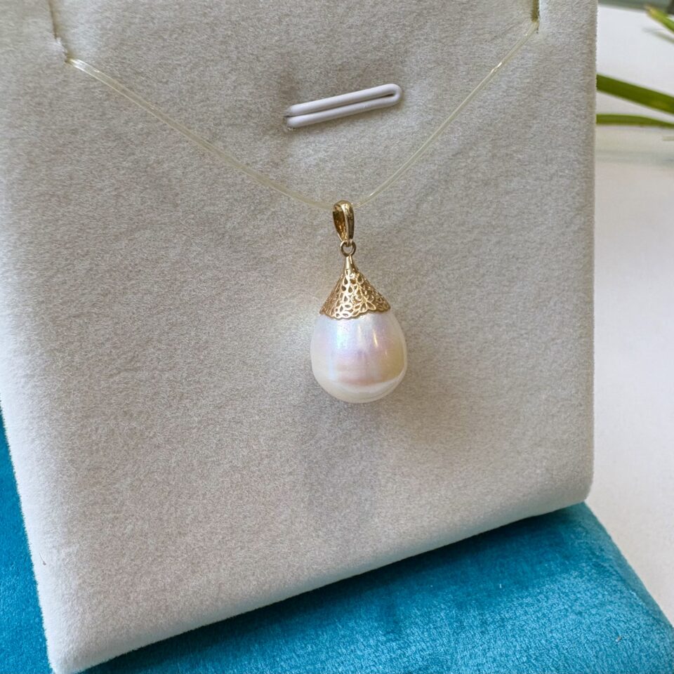 Ce pendentif s’articule autour d’une magnifique perle de culture blanche de taille 12-13mm. Sa forme baroque en goutte d’eau (ou « poire ») est rare et précieuse, évoquant à la fois une larme de lumière et une goutte de rosée